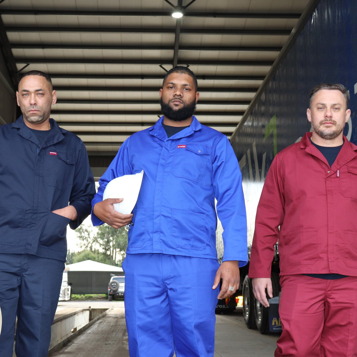 Three men in work uniforms walking in front of a truck with branding.