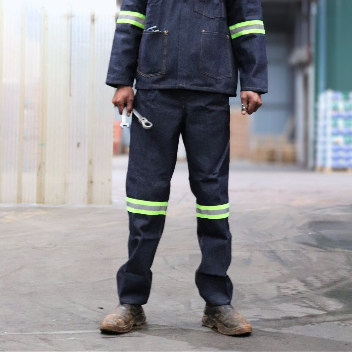 Person wearing a denim blue work overall with reflective stripes in an industrial setting.