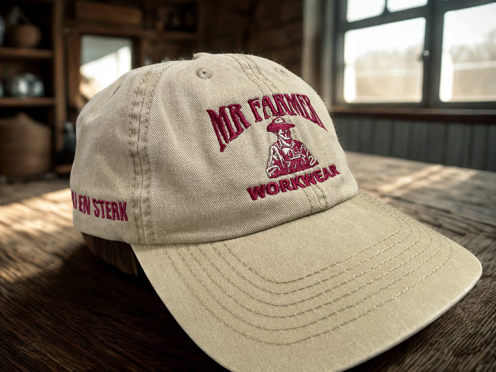 Khaki cap with red 'Mr. Farmer Workwear' logo on a wooden surface.
