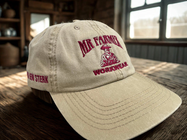 Khaki cap with red 'Mr. Farmer Workwear' logo on a wooden surface.